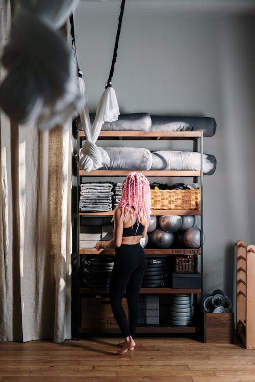 Woman in Black Leggings Standing Beside Brown Wooden Shelf