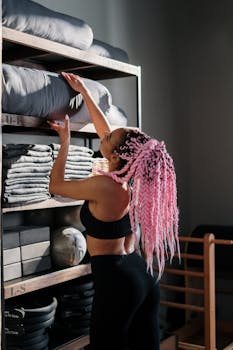 Yoga instructor with pink braided hair arranging yoga mats in a studio.