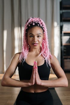 A woman with vibrant pink hair practices yoga indoors, focusing on relaxation and wellness.