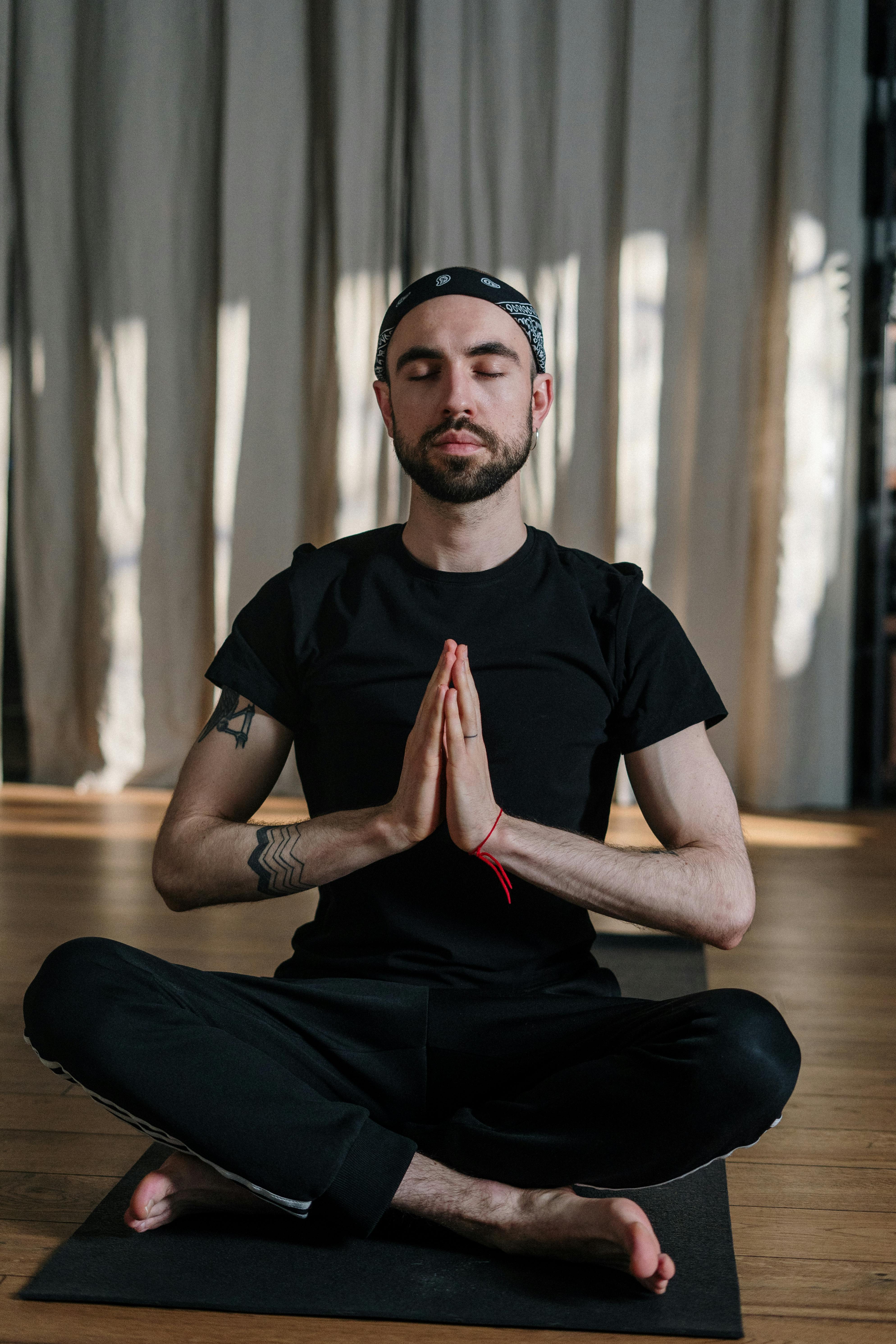 Man in Black Crew Neck T-shirt and Black Pants Sitting on Brown Wooden Floor