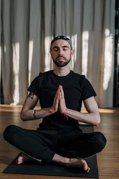 Relaxed man meditating indoors in a lotus pose, promoting wellness and calm.