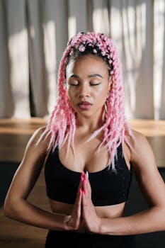 A woman practicing yoga indoors with vibrant pink hair, embodying peace and wellness.