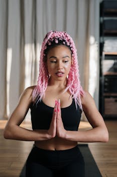 A young woman with pink hair meditating in a yoga studio, focusing on wellness and relaxation.