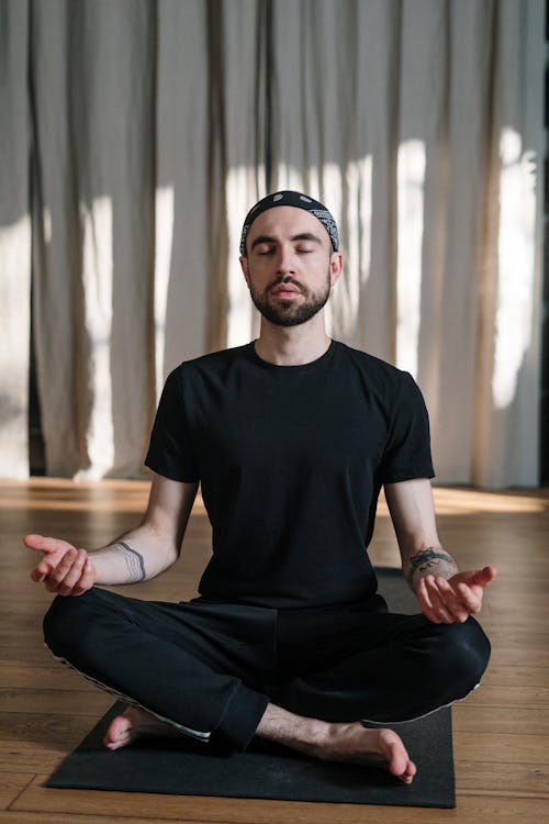 Man in Black Crew Neck T-shirt and Black Pants Sitting on Brown Wooden Floor