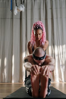 Yoga instructor with pink hair assisting a male student in a studio session, focused on wellness.