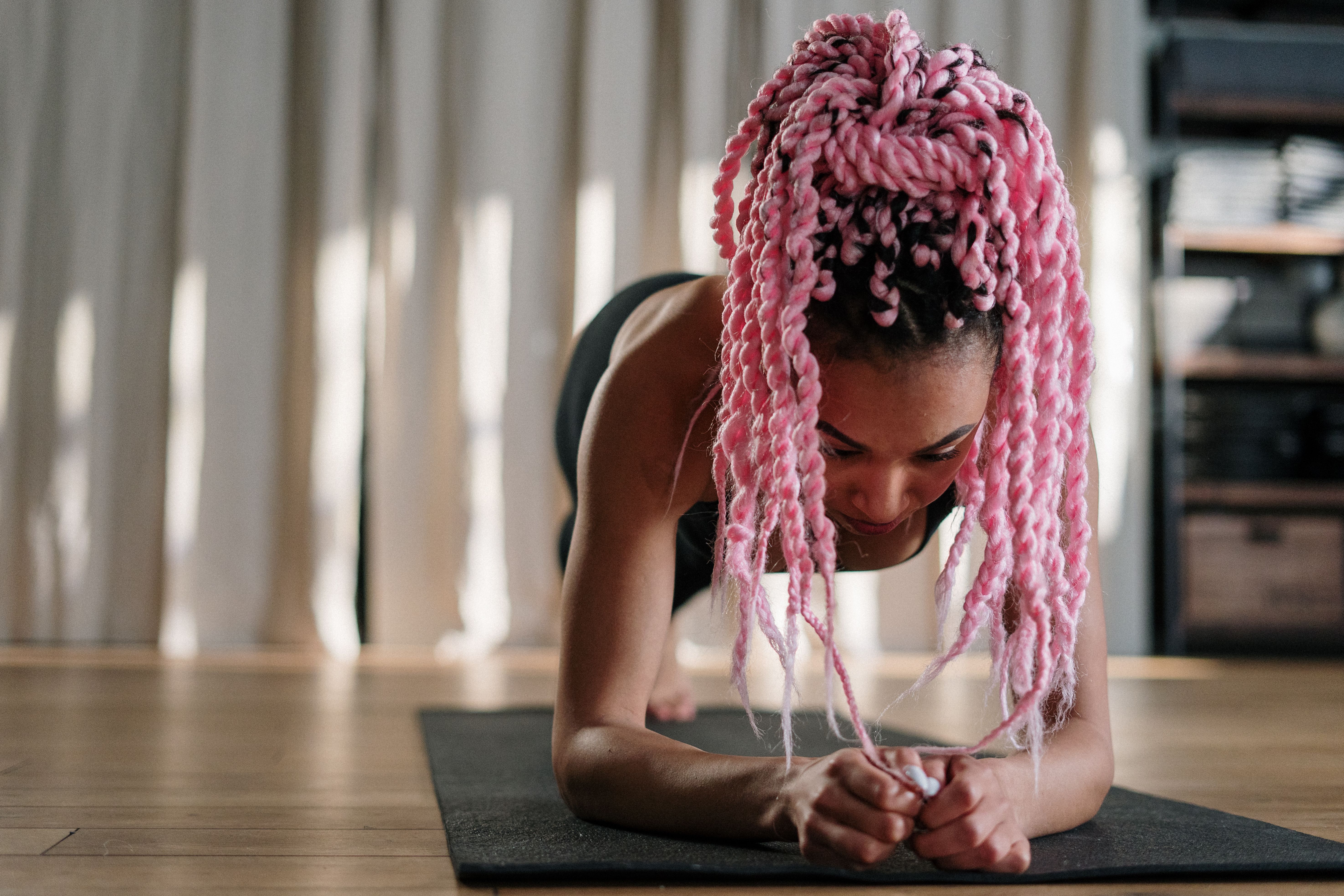 Woman with vibrant pink hair practicing yoga indoors, showcasing strength and balance.