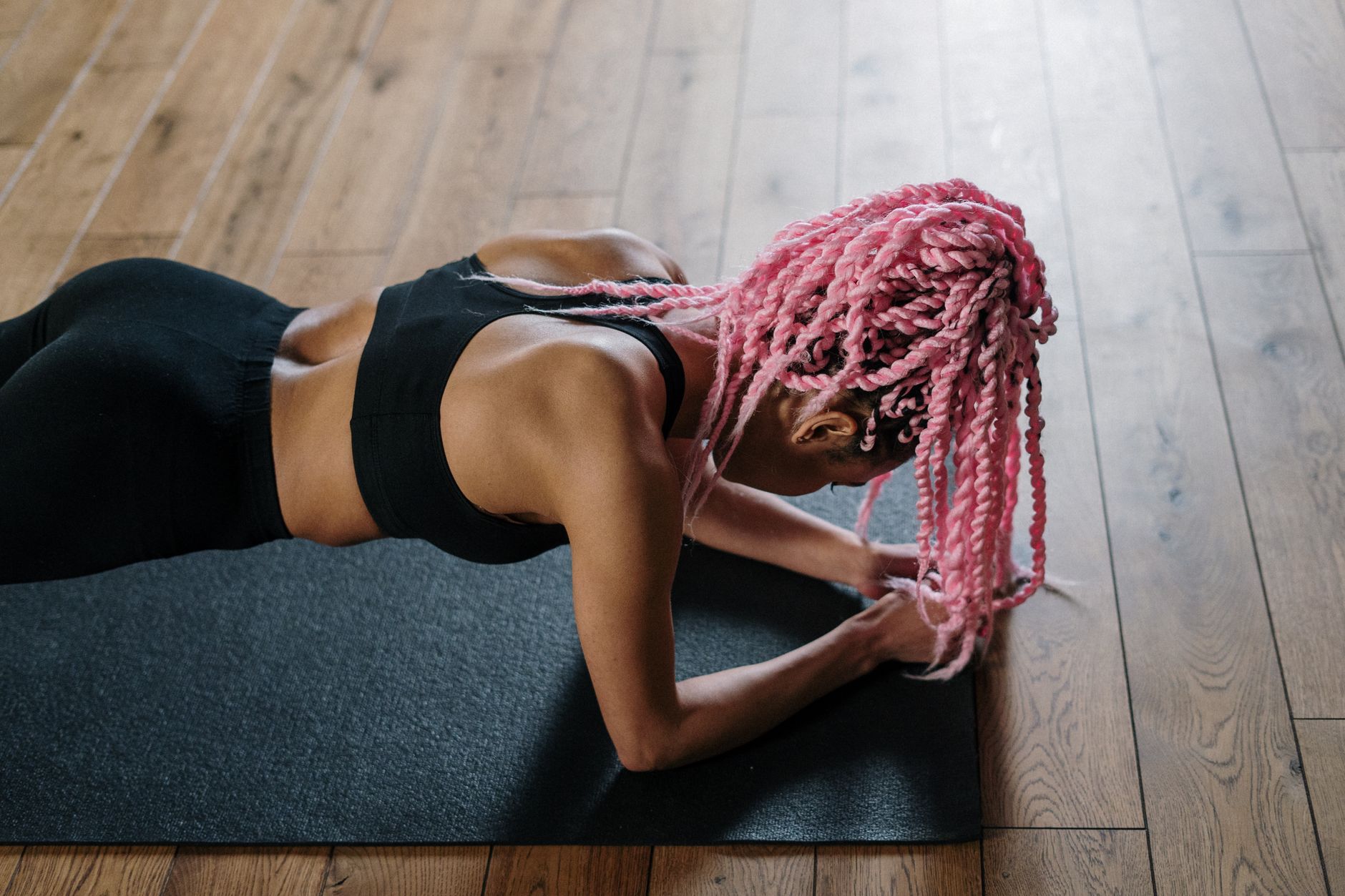 A woman with pink braided hair doing yoga indoors, showcasing fitness and wellness.
