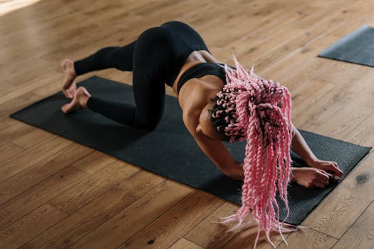 A woman with pink hair practicing yoga in a studio, focusing on strength and flexibility.
