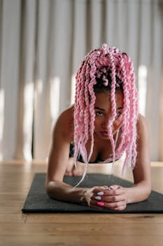 Focused woman with pink hair practicing yoga plank position on mat indoors.