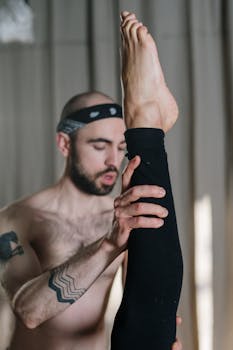 A yoga instructor assists a student in a deep stretch during a class, focusing on fitness and flexibility.