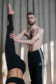 Male yoga instructor assisting a participant in a yoga studio, focusing on form and balance.