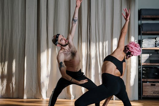 Two individuals engaging in a yoga session, showcasing strength and flexibility in a modern studio.