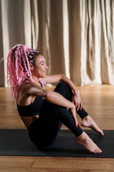 Woman with pink hair performing yoga in a studio, embodying health and wellness.