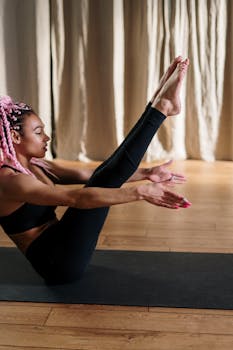 Black woman practicing yoga indoors with pink hair, emphasizing fitness and wellbeing.