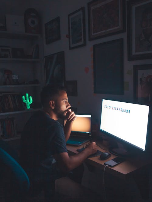 Pensive man watching images on computer screen in dark room