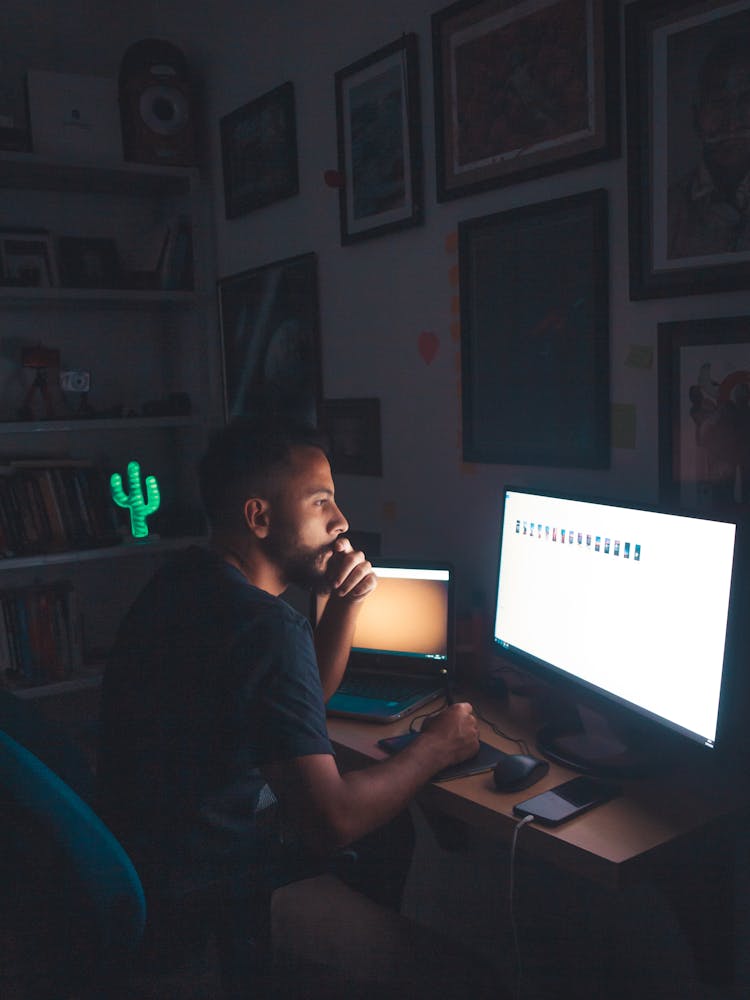 Pensive Man Watching Images On Computer Screen In Dark Room