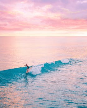 A surfer catching waves during a stunning sunset in Honolulu, Hawaii, showcasing vibrant ocean colors.
