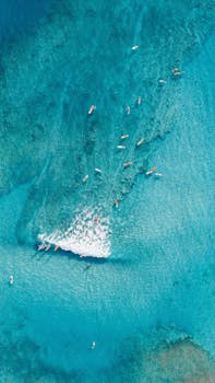 Stunning aerial shot of surfers riding turquoise waves in Hawaii, showcasing the beauty of the ocean and vibrant waters.
