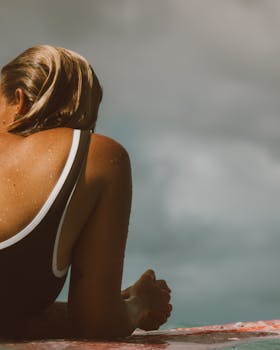 Photo by Jess Loiterton A woman lying on a surfboard in a bathing suit, enjoying the sunny Hawaiian beach.