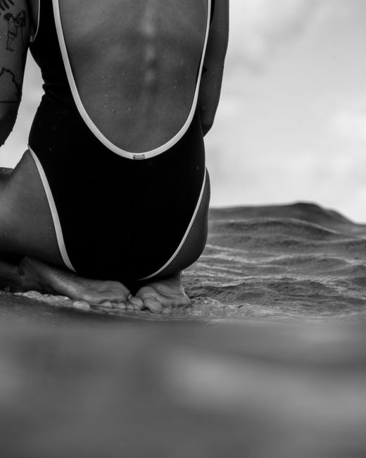 Black and white photo of a woman sitting on a beach in a swimsuit, offering a serene coastal vibe.