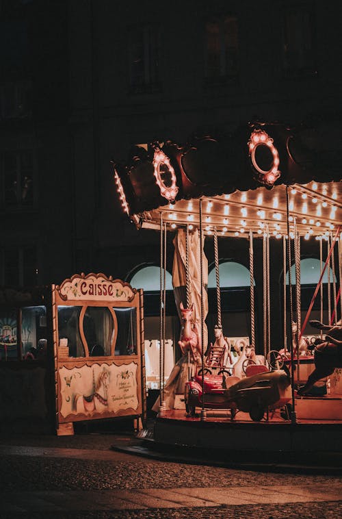 Shining carousel near ticket office on pavement in city at night in amusement park