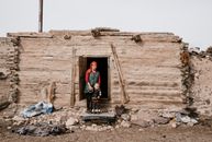 Ethnic woman standing with little boy near entrance in ruined old building in countryside and looking away while holding hand of little child