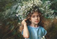 Thoughtful girl with chaplet standing near greenery
