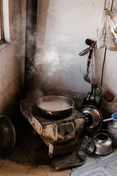 From above of metal pan with hot water placed on metal stove near placed metal kettle and utensil in poor kitchen