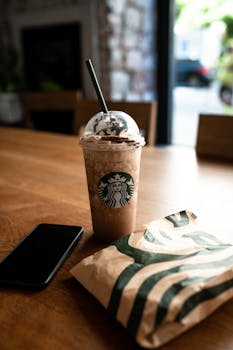 Iced coffee and pastry from Starbucks on a wooden table with a smartphone.