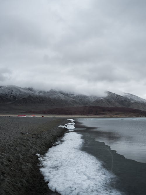 Picturesque landscape of frozen lake with snowy against calm mountain ridge in cloudy day