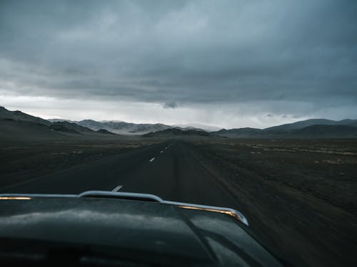 Asphalt road running away to remote mountains in haze and prairie seen from car in cloudy day