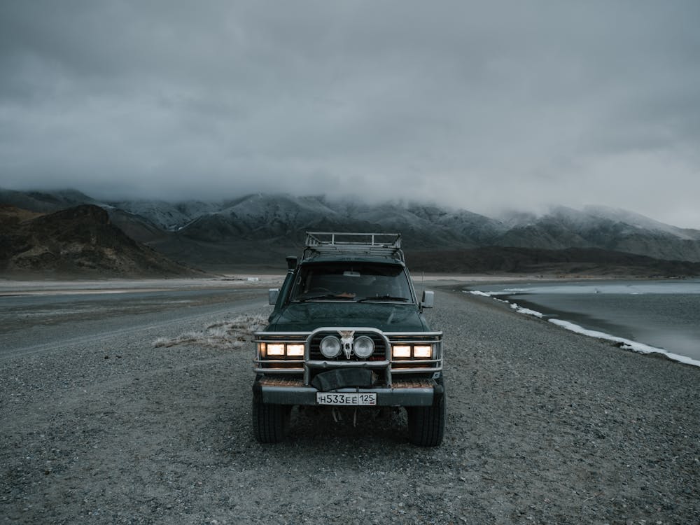 Free SUV automobile with headlights on parked on sand beach near ocean and ridge covered with mist in evening time Stock Photo