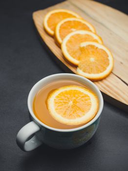 在黑暗背景的木板上，温暖的柑橘茶与新鲜切片的橙子摆在一起