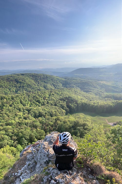 Free Anonymous male traveler resting on cliff edge against mountainous terrain Stock Photo