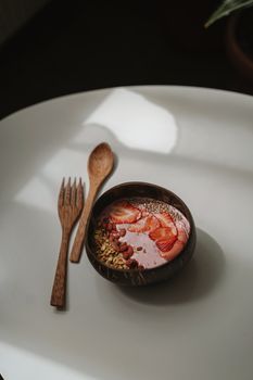 白色桌子的木碗里，盛着美味的草莓冰沙，上面撒有种子和燕麦