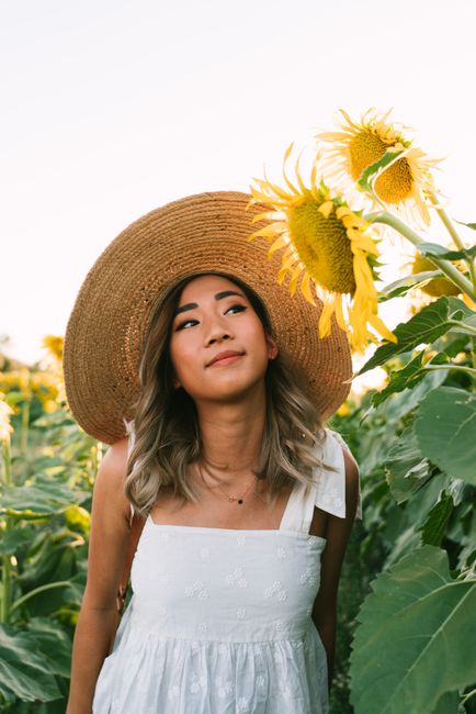 A woman wearing a sunhat stands among blooming sunflowers, capturing a serene summer vibe.