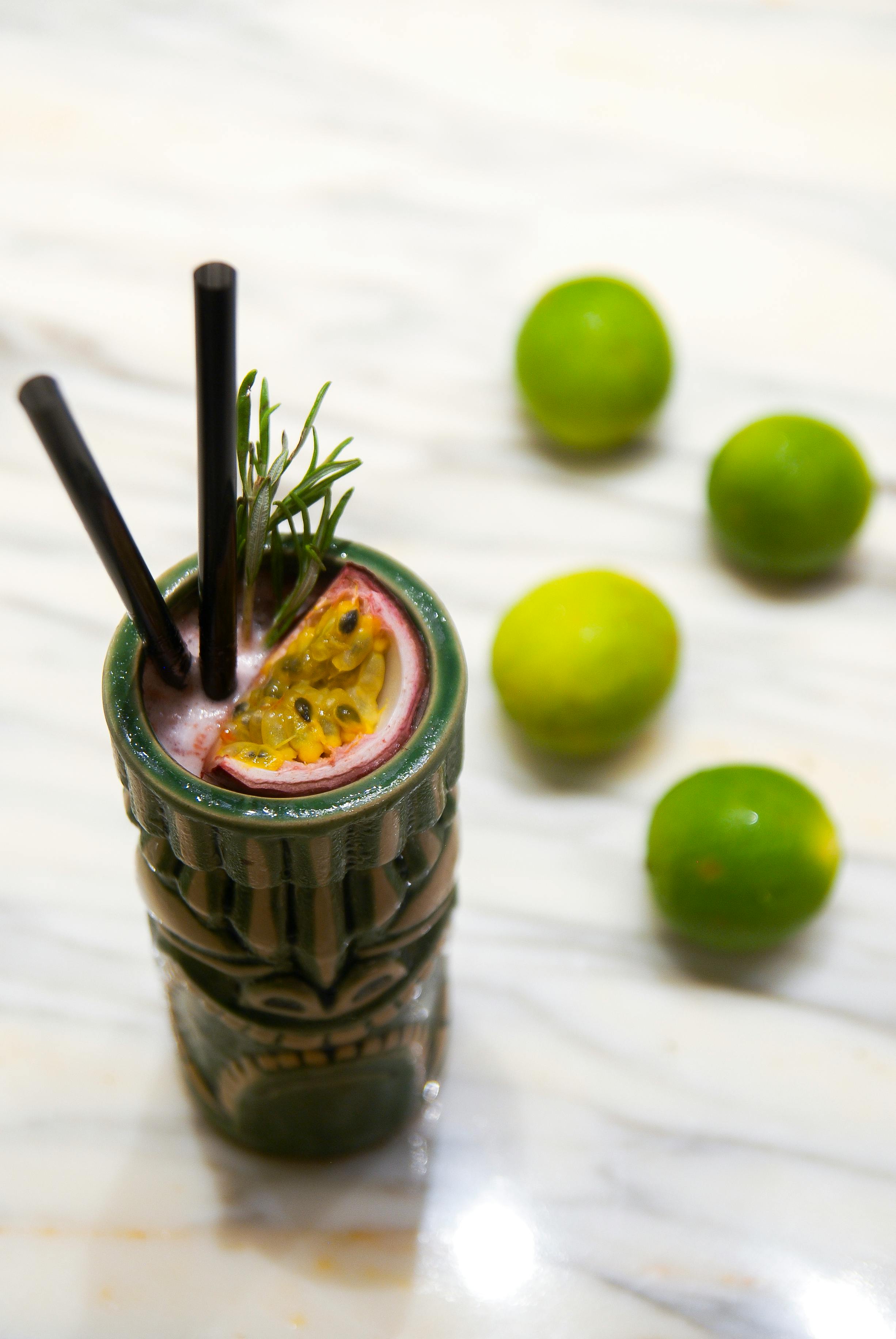Refreshing tropical cocktail in a tiki mug with passion fruit and limes on a marble surface.