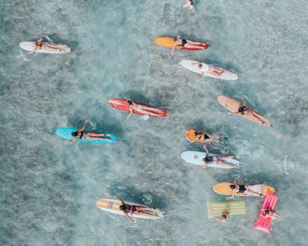Aerial photo of surfers in Hawaii paddling on colorful boards in clear ocean water.