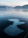 Majestic view of icy river with formed spots on cold surface near high mounts under cloudy sky in daylight
