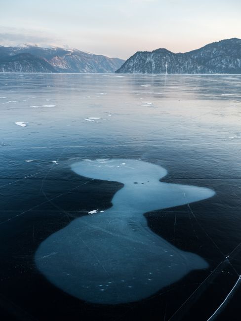 Majestic view of icy river with formed spots on cold surface near high mounts under cloudy sky in daylight