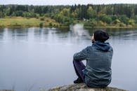 一个人坐在湖边的岩石上，抽着烟，被大自然的宁静所包围