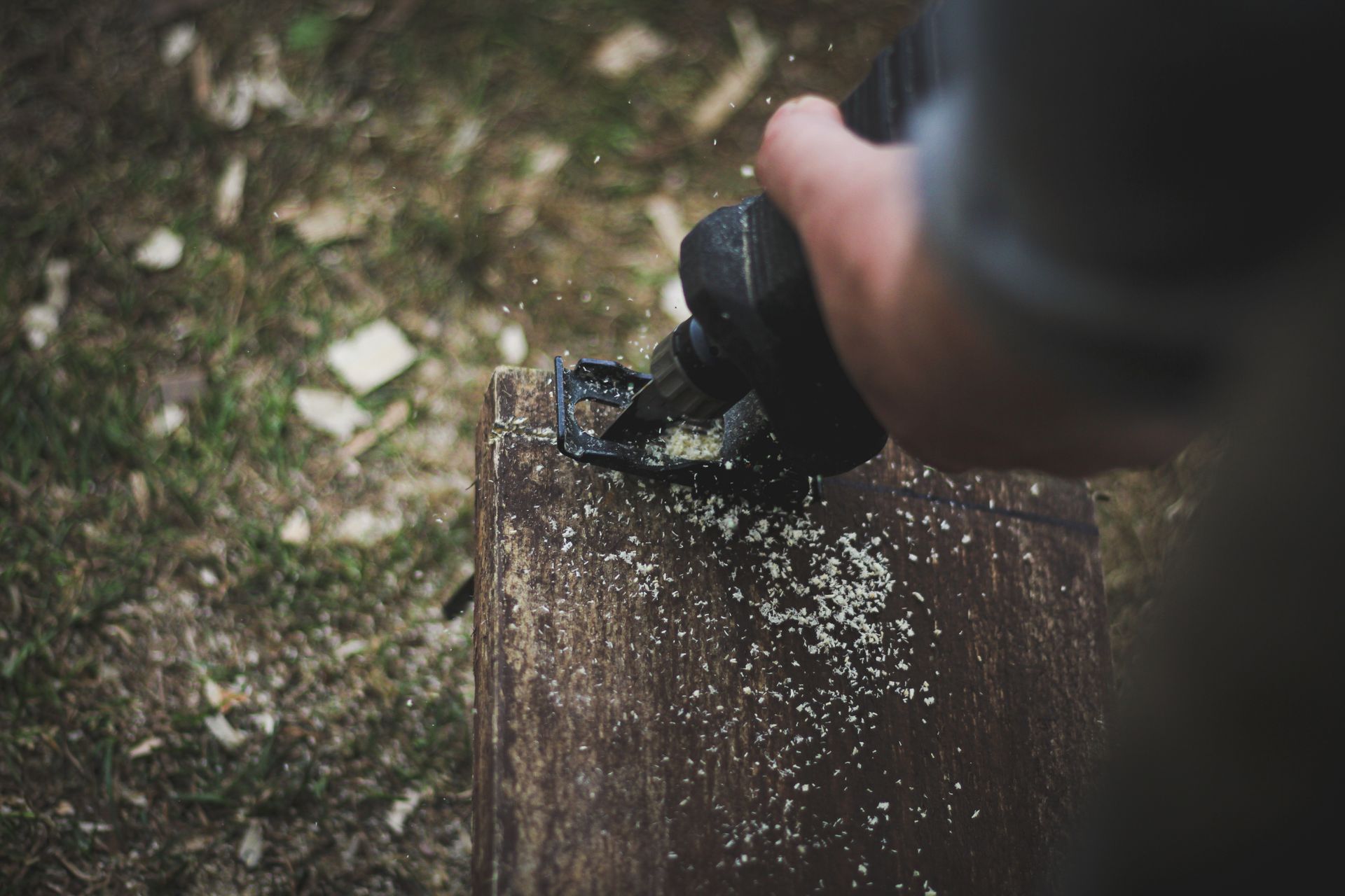 A man uses a power tool for wood cutting, creating sawdust outdoors.