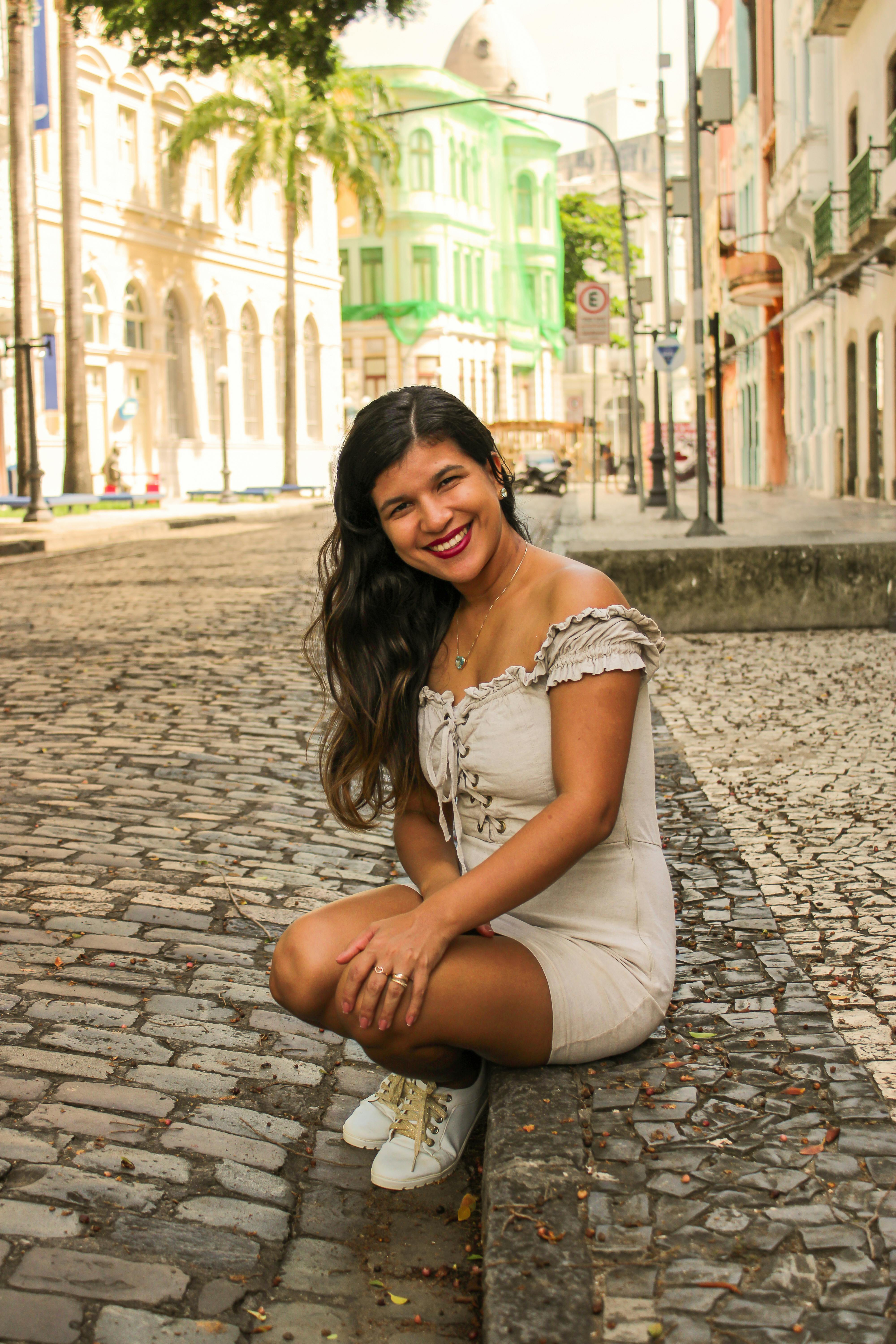 A cheerful woman poses on a historic cobblestone street in Recife, Brazil, showcasing urban summer fashion.