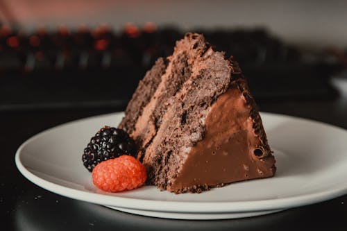 Appetizing sweet dark chocolate cake served on white plate and decorated with ripe black and red blackberries
