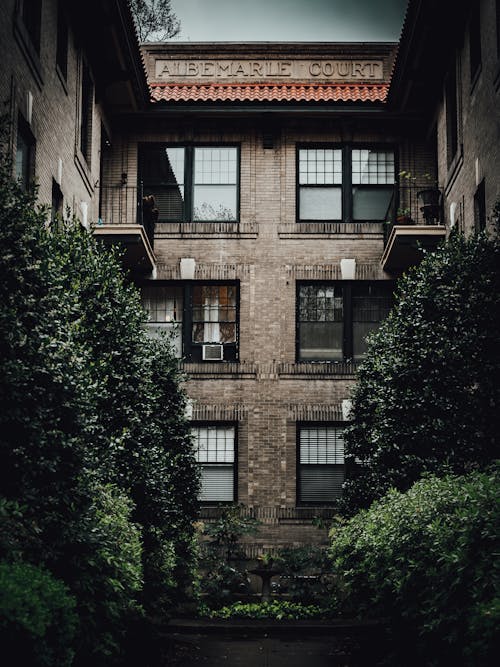 Quiet patio of aged apartment brick building decorated with ornamental small fountain and green abundant trees