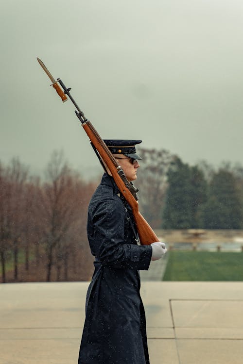 Serious soldier with rifle on shoulder marching in park