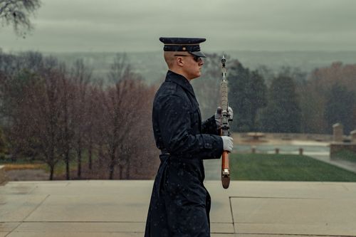 Free Side view concentrated serious soldier wearing cap and coat marching with rifle during solemn ceremony in autumn park Stock Photo