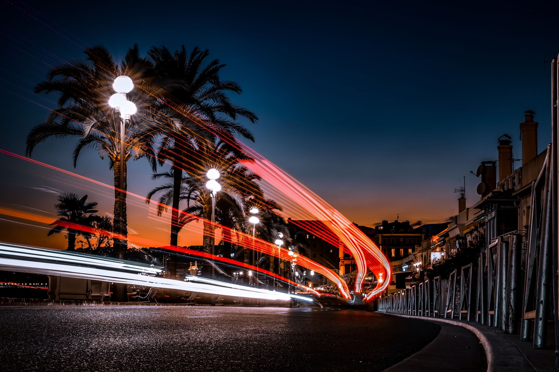 Vibrant night view of Nice, France featuring dynamic car light trails along palm-lined streets.