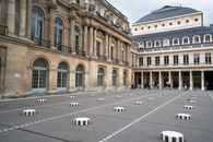 Inner courtyard of Palais Royal with ornamental windows and Columns of Buren on ground with tourists visiting sight on summer day