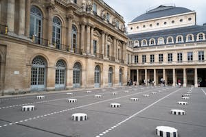 Inner courtyard of Palais Royal with ornamental windows and Columns of Buren on ground with tourists visiting sight on summer day
